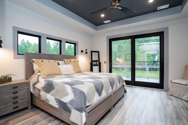 bedroom featuring access to exterior, light hardwood / wood-style floors, a raised ceiling, and ceiling fan