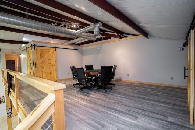 dining space featuring wood-type flooring, a barn door, and beam ceiling