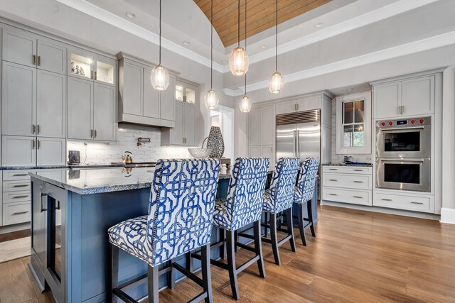 kitchen featuring appliances with stainless steel finishes, a kitchen breakfast bar, hanging light fixtures, light stone countertops, and light hardwood / wood-style flooring