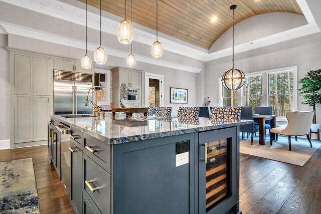 kitchen featuring wine cooler, stainless steel built in fridge, a kitchen island with sink, and hanging light fixtures