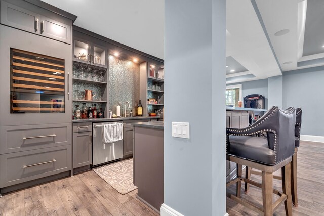 bar featuring sink, gray cabinetry, stainless steel dishwasher, a raised ceiling, and light wood-type flooring