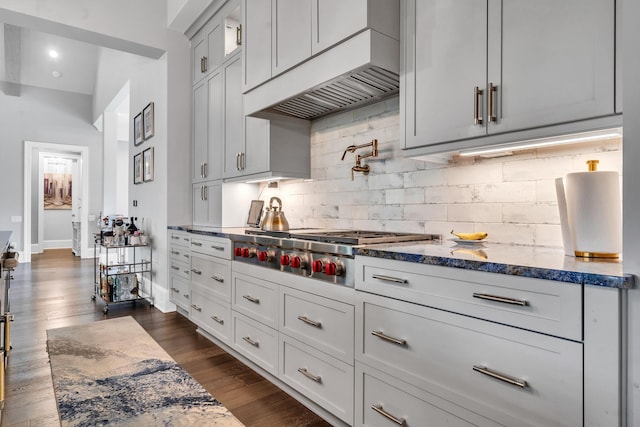 kitchen featuring custom exhaust hood, dark hardwood / wood-style flooring, stainless steel gas stovetop, light stone countertops, and backsplash