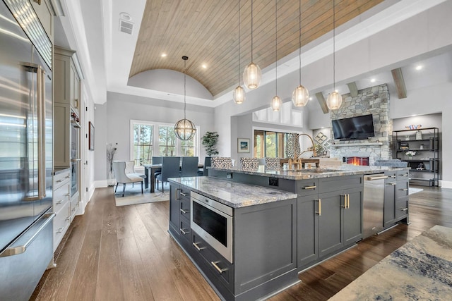 kitchen with a spacious island, built in appliances, dark wood-type flooring, and hanging light fixtures