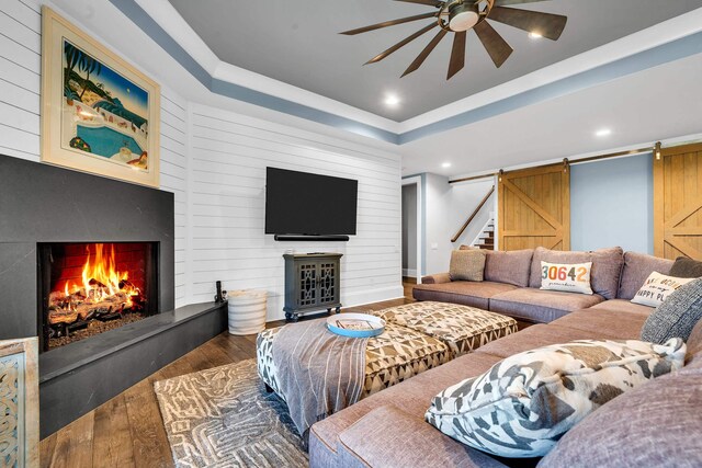 living room with ceiling fan, wood-type flooring, a barn door, and a tray ceiling