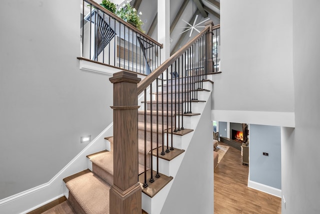 staircase with beam ceiling, wood-type flooring, and high vaulted ceiling