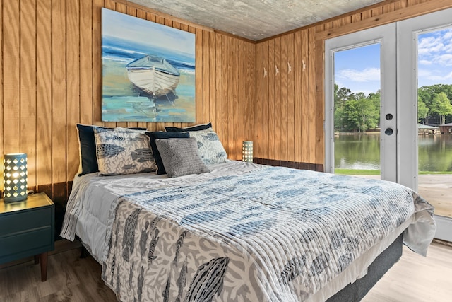 bedroom with wood finished floors, wooden walls, access to outside, a water view, and french doors