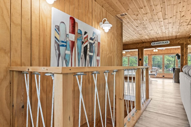 hallway featuring wooden walls, visible vents, wood ceiling, and wood finished floors