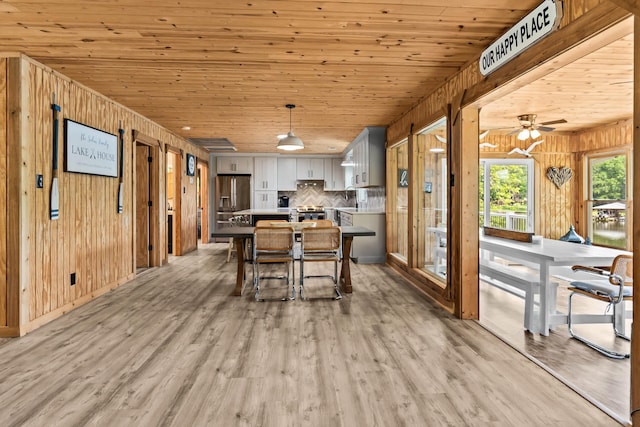 kitchen with wood walls, wood ceiling, light wood finished floors, backsplash, and stainless steel appliances