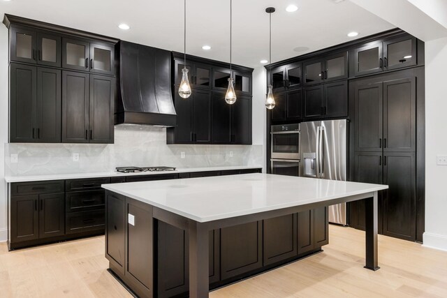 1050 Carnoustie Dr, Greensboro, GA 30642 - kitchen with stainless steel appliances, premium range hood, a kitchen island, decorative backsplash, and light wood-style flooring