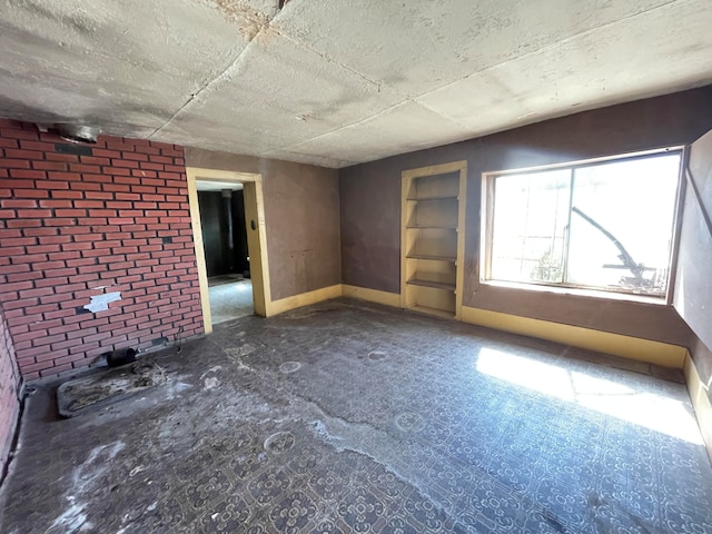 spare room with built in features, brick wall, and dark colored carpet