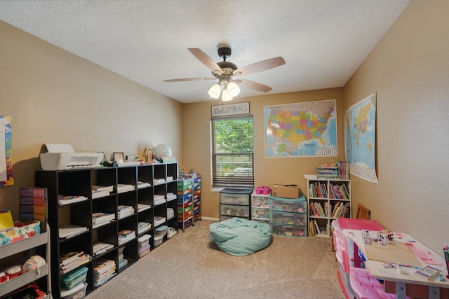 recreation room featuring a textured ceiling, light colored carpet, and ceiling fan