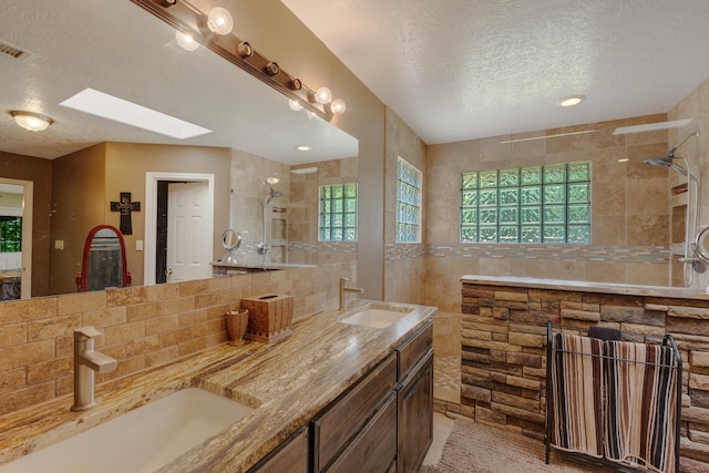 bathroom with a skylight, double vanity, a textured ceiling, tasteful backsplash, and tile walls