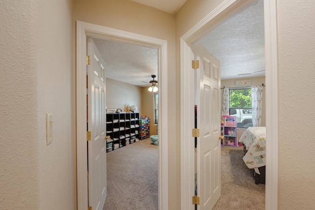 hall featuring light carpet and a textured ceiling