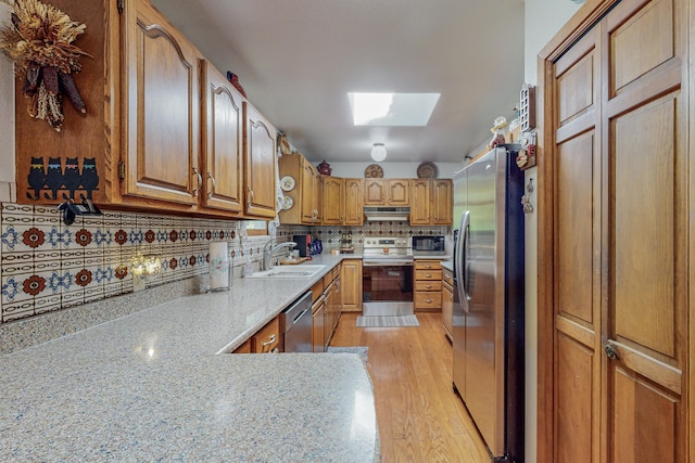 kitchen featuring light wood-type flooring, light stone counters, stainless steel appliances, a skylight, and sink