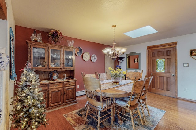 dining room featuring a skylight, a notable chandelier, a baseboard radiator, and light hardwood / wood-style floors