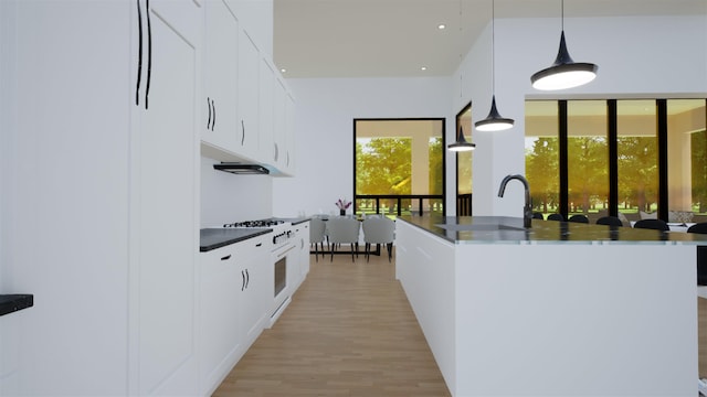 kitchen featuring hanging light fixtures, high end stove, white cabinets, and a center island with sink