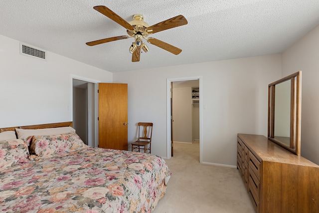 carpeted bedroom featuring a walk in closet, a textured ceiling, a closet, and ceiling fan