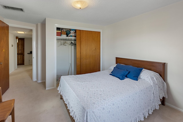 bedroom with a textured ceiling, light colored carpet, and a closet