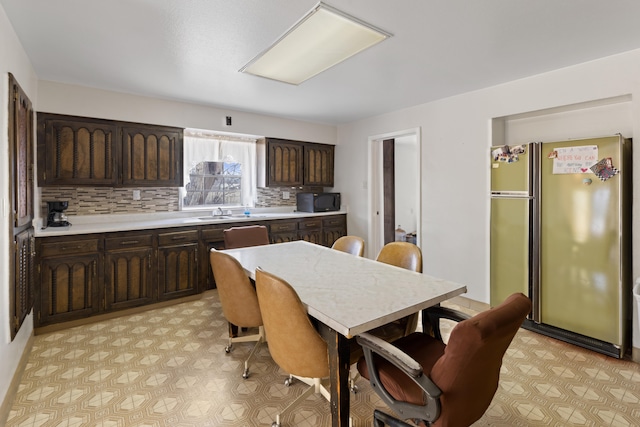 kitchen featuring backsplash, light tile flooring, sink, dark brown cabinetry, and stainless steel refrigerator