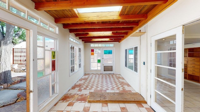 unfurnished sunroom featuring a skylight, beam ceiling, plenty of natural light, and french doors