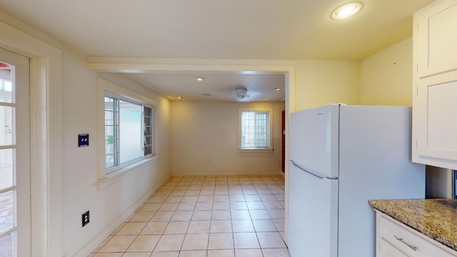 kitchen featuring light tile flooring, white refrigerator, white cabinetry, and light stone counters