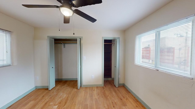 unfurnished bedroom with two closets, ceiling fan, and light hardwood / wood-style flooring