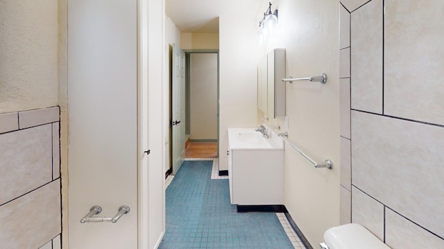 bathroom featuring toilet, vanity with extensive cabinet space, tile floors, and tile walls