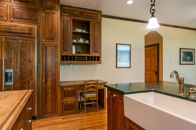 kitchen with pendant lighting, built in desk, sink, wooden counters, and light wood-type flooring