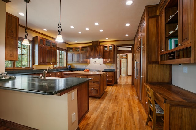 kitchen with pendant lighting, sink, ornamental molding, custom range hood, and a center island with sink