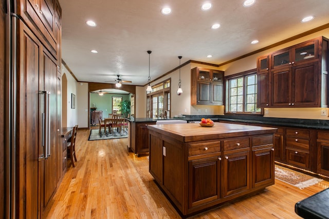 kitchen with pendant lighting, crown molding, light hardwood / wood-style flooring, paneled built in refrigerator, and a center island