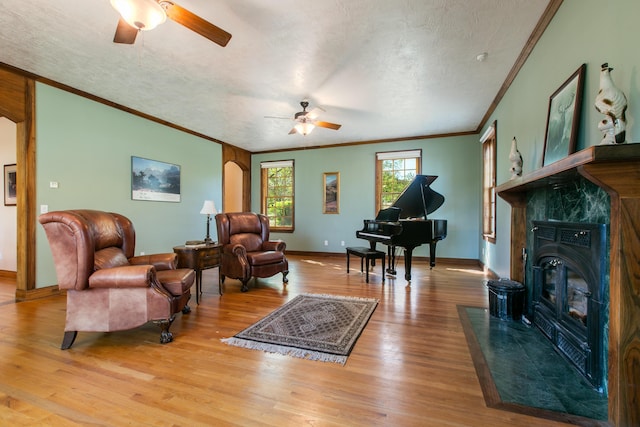 living area with ceiling fan, ornamental molding, light hardwood / wood-style floors, and a textured ceiling