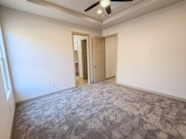 carpeted empty room featuring ceiling fan and a raised ceiling