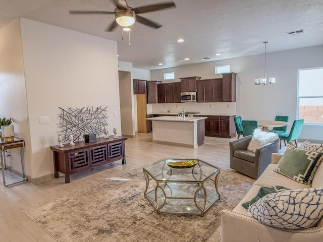 living room featuring sink, ceiling fan with notable chandelier, light hardwood / wood-style flooring, and a textured ceiling