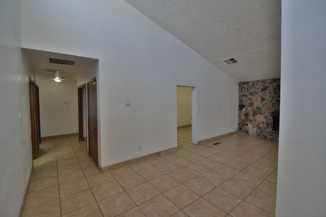 empty room featuring high vaulted ceiling, a textured ceiling, and light tile patterned floors