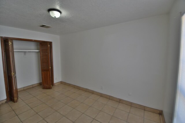 unfurnished bedroom with a textured ceiling, light tile patterned floors, and a closet