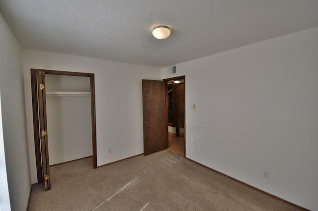 unfurnished bedroom featuring a textured ceiling, light colored carpet, and a closet