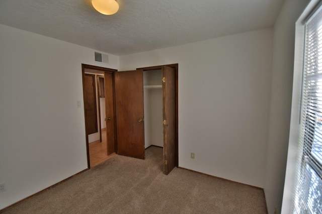 unfurnished bedroom with light carpet, a textured ceiling, and a closet