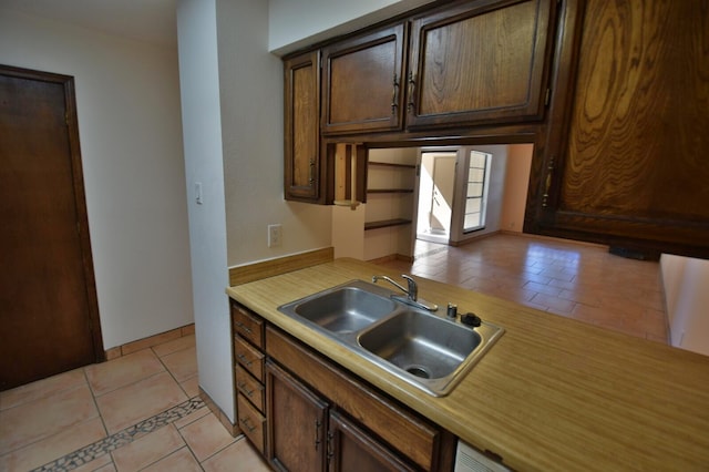 kitchen with dark brown cabinetry, light tile patterned flooring, and sink