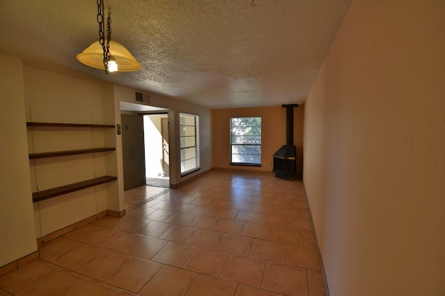 empty room featuring a wood stove, a textured ceiling, and light tile patterned flooring