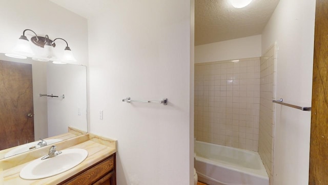 bathroom featuring a textured ceiling, tiled shower / bath combo, and vanity