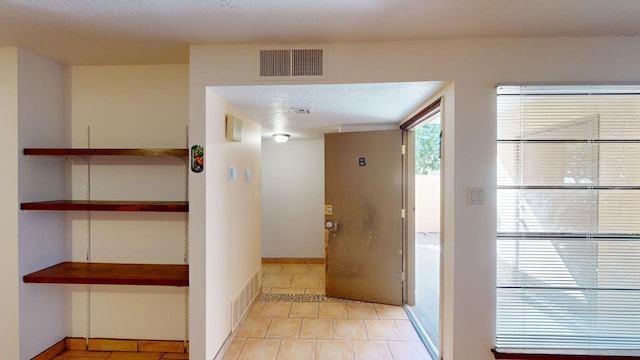 corridor featuring a textured ceiling and light tile patterned floors