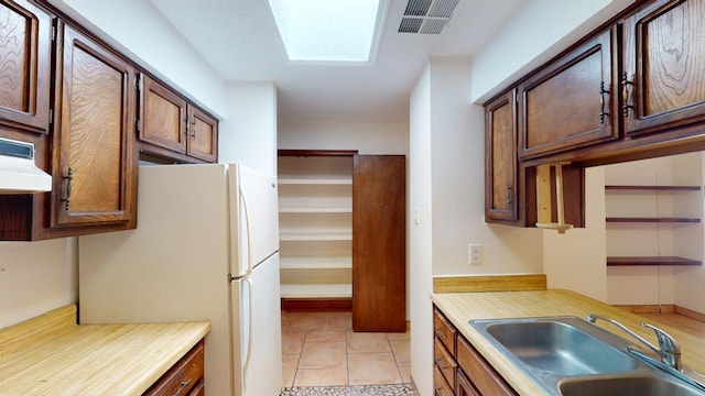 kitchen featuring white refrigerator, light tile patterned floors, ventilation hood, a skylight, and sink