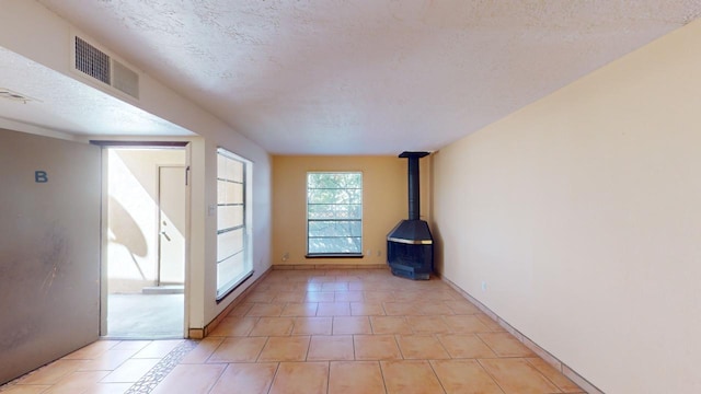 interior space featuring a textured ceiling, light tile patterned floors, and a wood stove