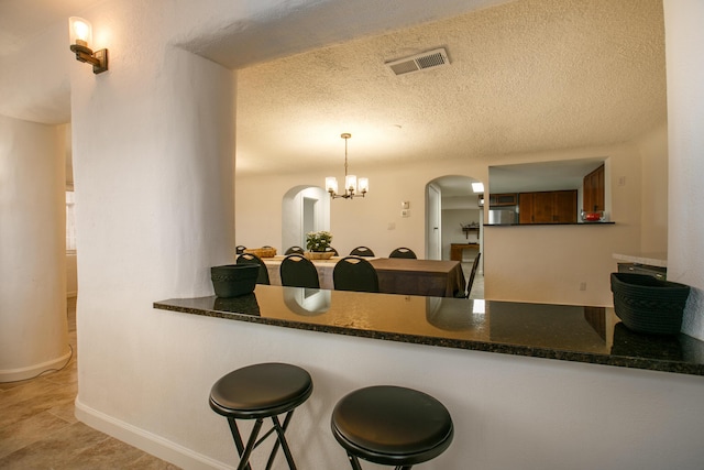 kitchen with a breakfast bar, a textured ceiling, kitchen peninsula, a notable chandelier, and pendant lighting