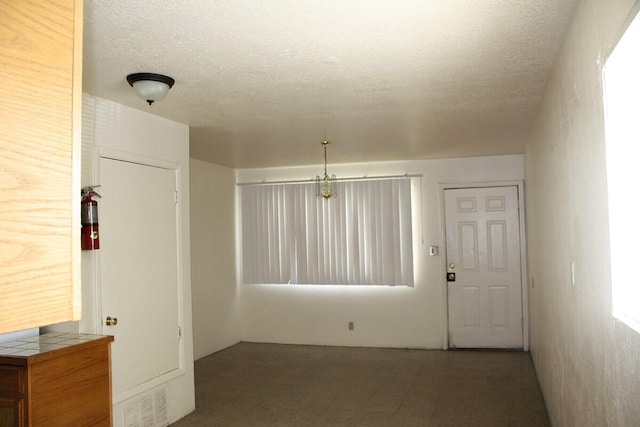 tiled empty room with a chandelier and a textured ceiling