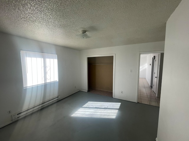 unfurnished bedroom with a spacious closet, a textured ceiling, a closet, and a baseboard heating unit