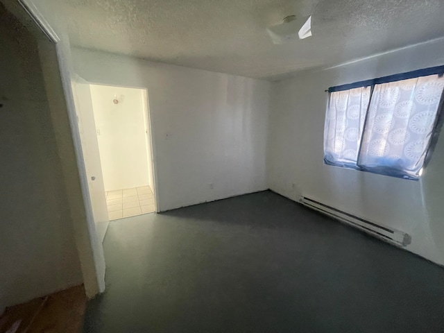 empty room featuring a textured ceiling, dark tile flooring, and a baseboard radiator