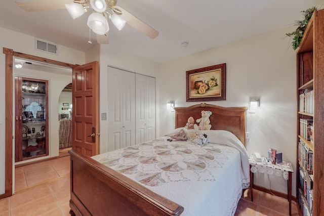 bedroom featuring arched walkways, light tile patterned floors, visible vents, a ceiling fan, and a closet