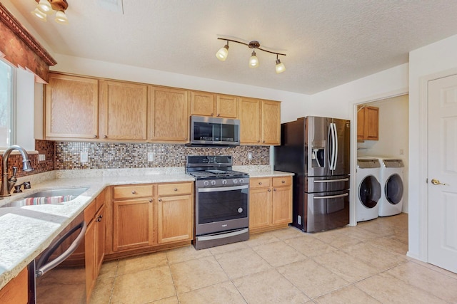 kitchen featuring independent washer and dryer, sink, stainless steel appliances, track lighting, and tasteful backsplash