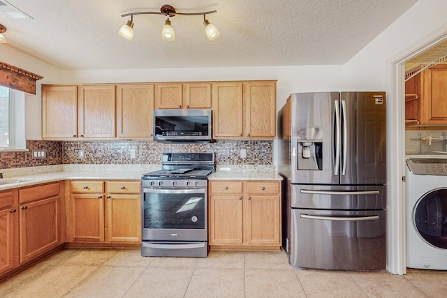 kitchen featuring backsplash, washer / dryer, stainless steel appliances, light tile floors, and a textured ceiling